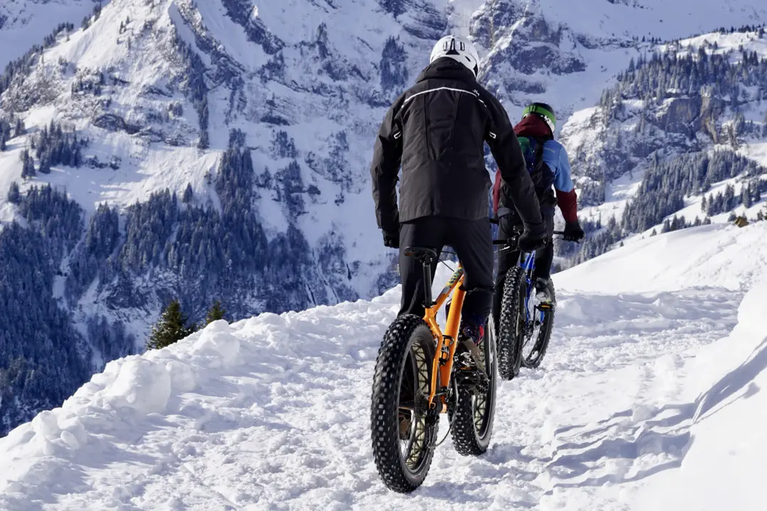 Ffatbiker on a winter trail with snowy mountains in the background